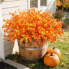 A vibrant display of orange and yellow artificial fall foliage in a wooden barrel planter with an orange pumpkin nearby.
