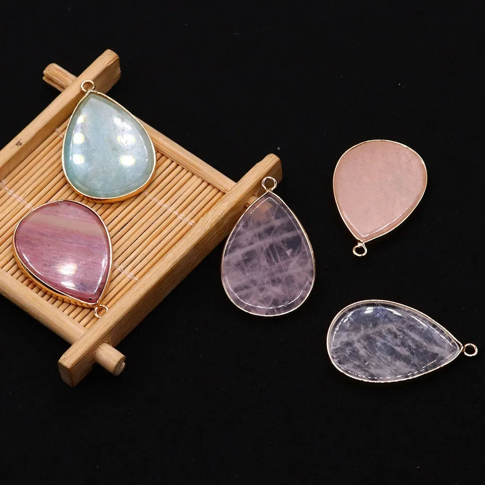A collection of five polished gemstone pendants, including blue-green and pink agate, displayed on a wooden tray.
