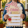 A young girl holds a personalized wooden sign for her first day of school featuring a daisy bow and various personal details.