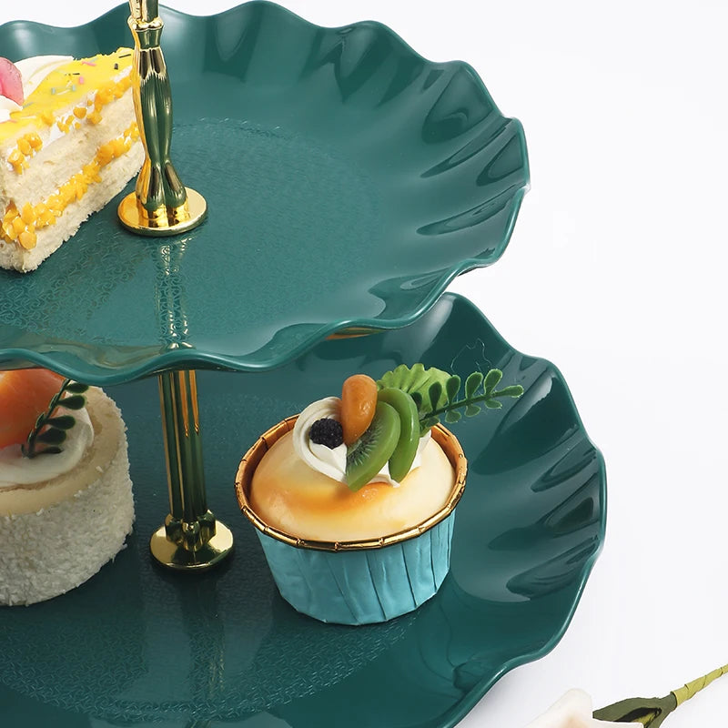 A two-tier serving stand holding a slice of cake and a small pastry on a dark green plate.