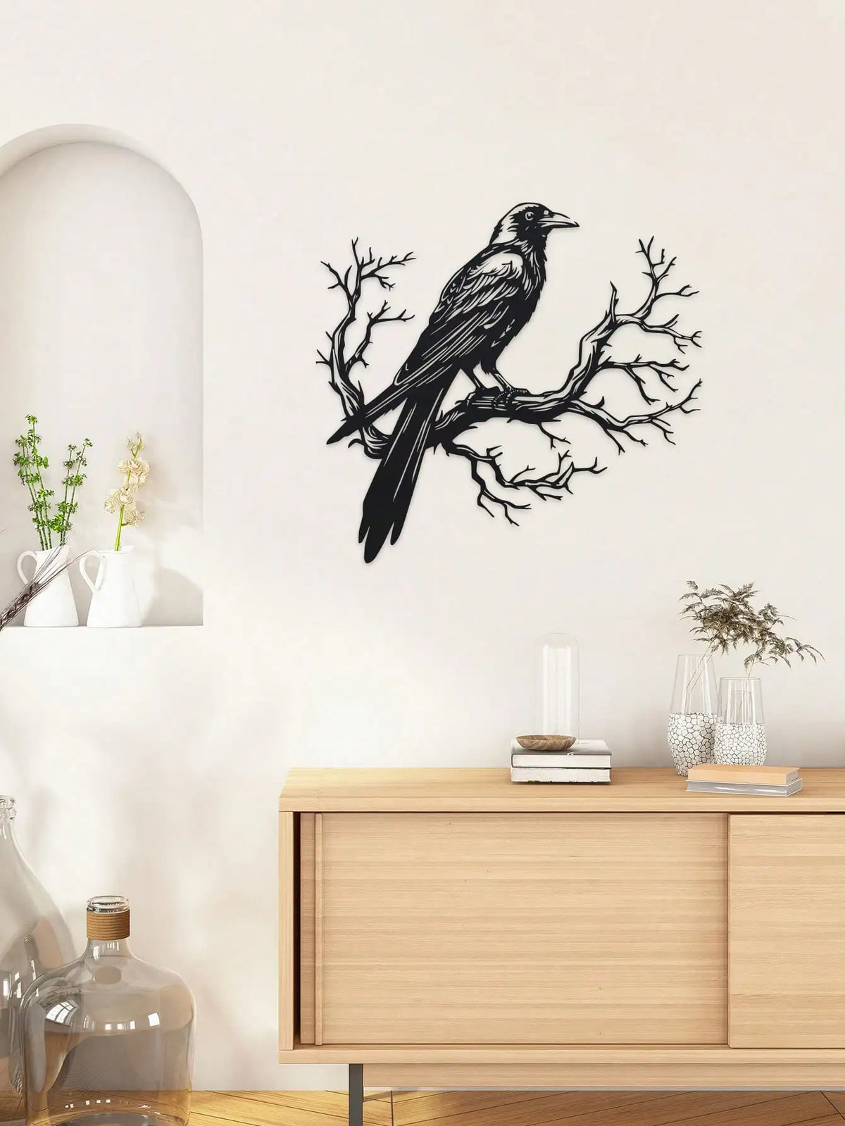 Black raven silhouette on a bare tree branch metal wall art hanging above a wooden cabinet.
