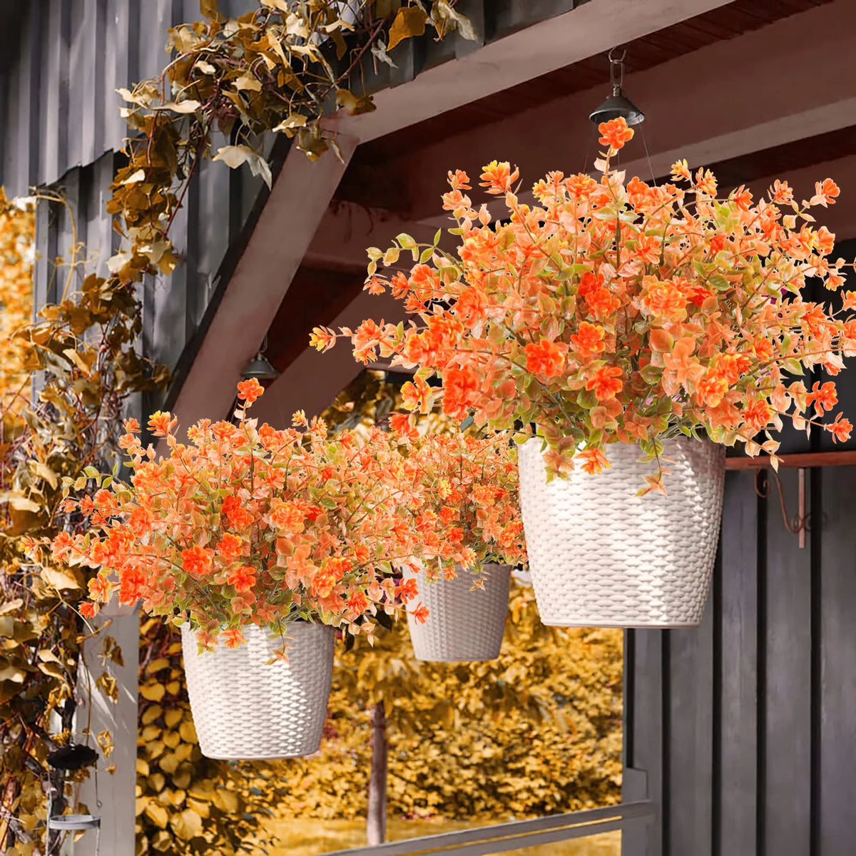 A hanging display of orange and yellow artificial daisies in white pots against a dark background.