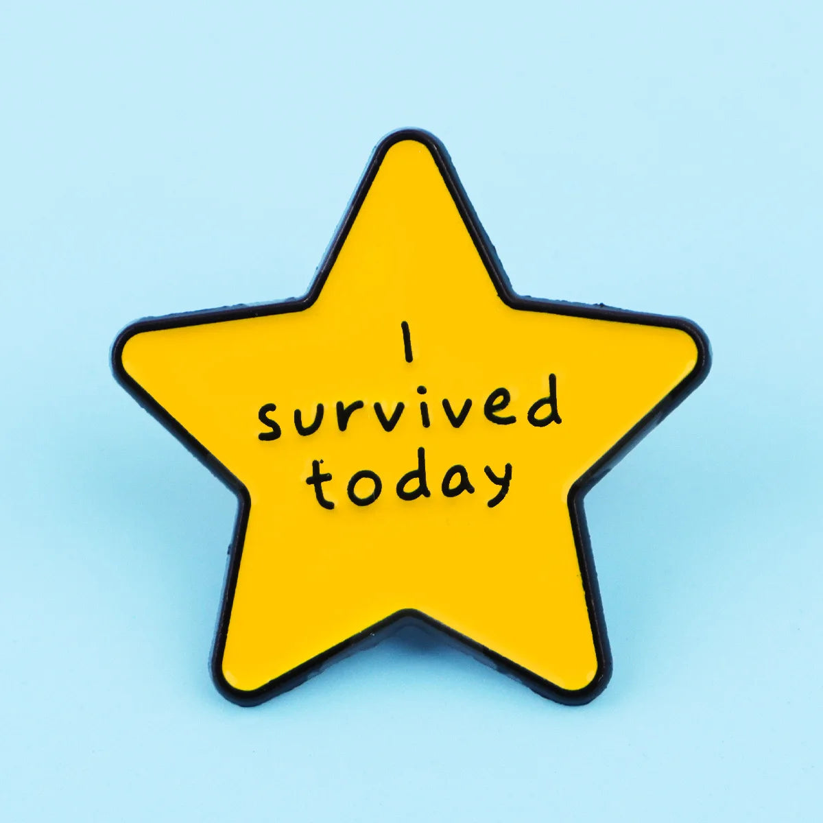 A yellow star enamel pin with black outline featuring the text I survived today.