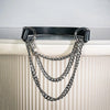 A triple-layer silver chain choker necklace with a black leather strap hanging against a white radiator.