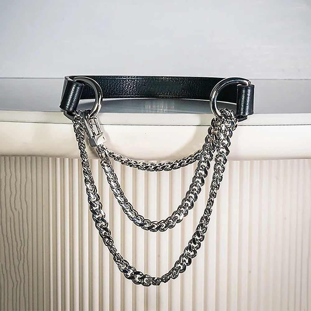 A triple-layer silver chain choker necklace with a black leather strap hanging against a white radiator.