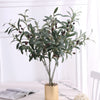 Artificial olive branch with dark fruits and green leaves displayed in a glass vase.