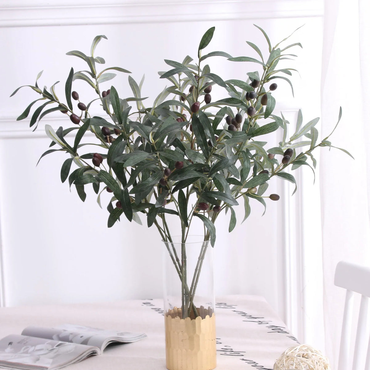 Artificial olive branch with dark fruits and green leaves displayed in a glass vase.