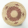 Round woven straw wall decor hanging with concentric spiral pattern in natural beige and reddish-brown tones