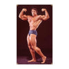 A muscular man posing with his arms flexed, wearing dark shorts, against a dark background.