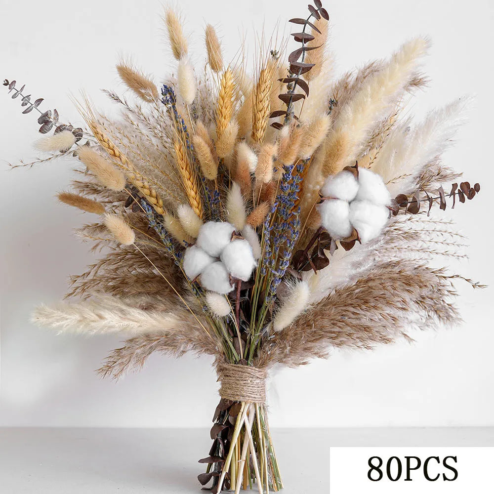 A dried flower bouquet featuring beige and tan grasses, blue accents, and white cotton balls tied together.