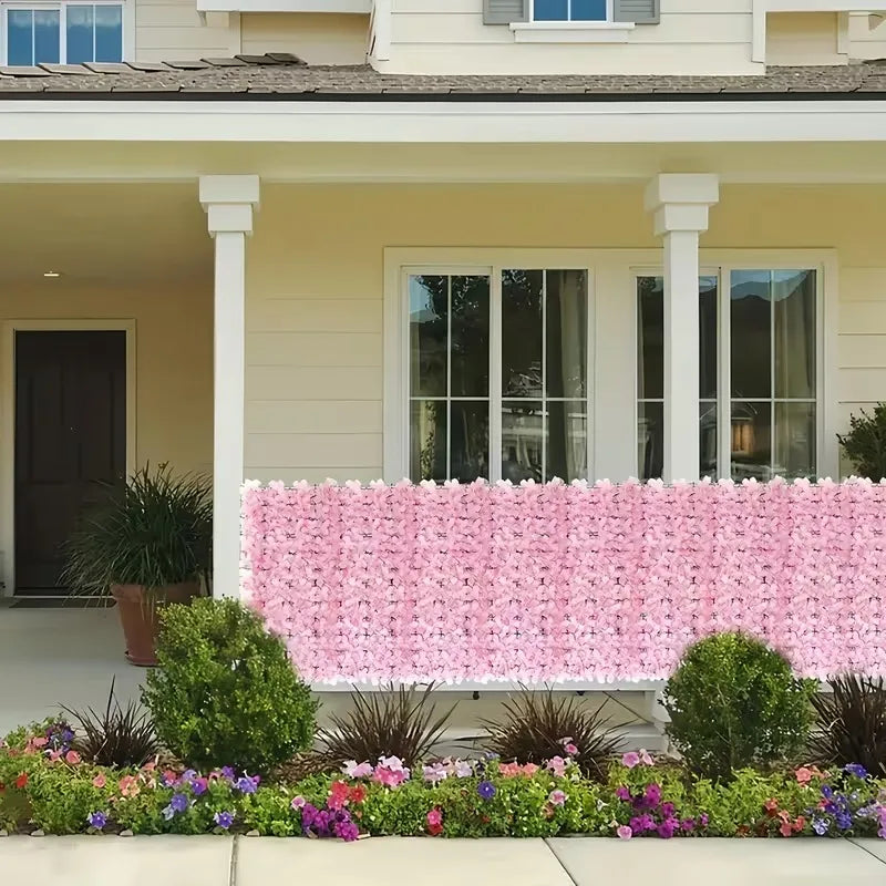 A pink artificial cherry blossom privacy fence screen in front of a light-colored house.