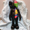 A black bear figurine with a green head and pink accents is displayed on a white textured cloth.