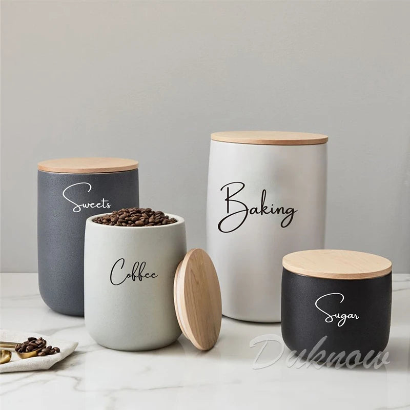 A collection of white and gray canisters with black script labels for sweets, coffee, baking, and sugar storage.