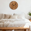 A bedroom scene featuring a minimalist wooden wall clock above a bed with white linens and natural wood furniture.