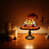 A witch hat night light with a stained glass effect illuminates a dark wooden surface next to candles and autumn leaves.