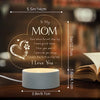 A warm glow night light featuring a heart-shaped sign with a message to Mom and a book in the background.