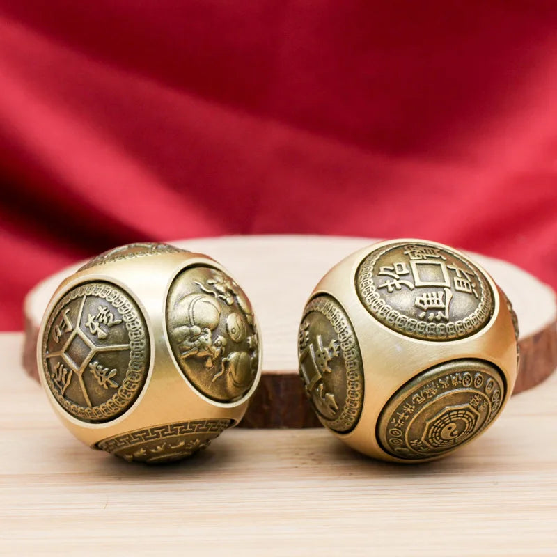 Two brass Chinese lucky coin spinners resting on a wooden surface with a red fabric background.
