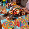 A vibrant Mexican fiesta disposable tableware set laid out on a wooden table with colorful patterned placemats and food.