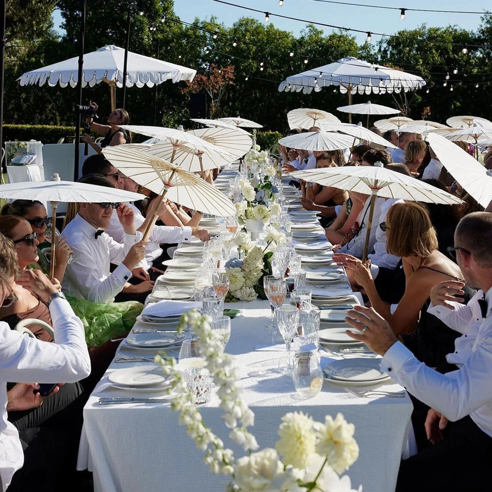 Guests seated at an outdoor event table under white umbrellas with decorative paper parasols.