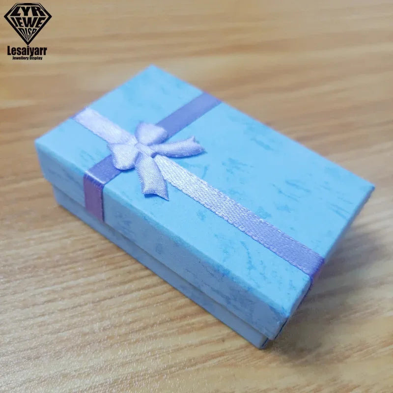 Una caja de regalo azul claro atada con una cinta lavanda sobre una superficie de madera.