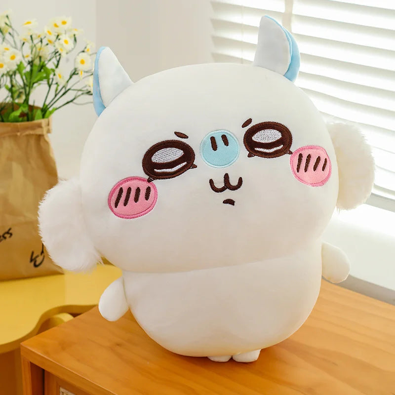 A white Usagi Chiikawa plush doll with blue ears and pink accents sitting on a wooden surface.