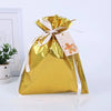 A gold foil drawstring gift bag with a white ribbon and a small tag featuring a gingerbread man and a snowman design.