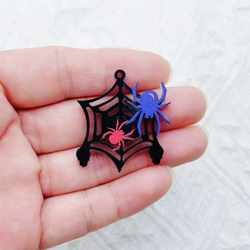 Una mano sostiene un dije de Halloween de acrílico negro con siluetas de araña y escorpión.