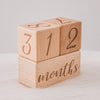 A stack of wooden baby milestone cards showing the numbers 3, 1, 2, and 2 on individual blocks.