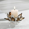A clear glass candle holder filled with dried lotus petals and a white pillar candle burning in a minimalist setting.