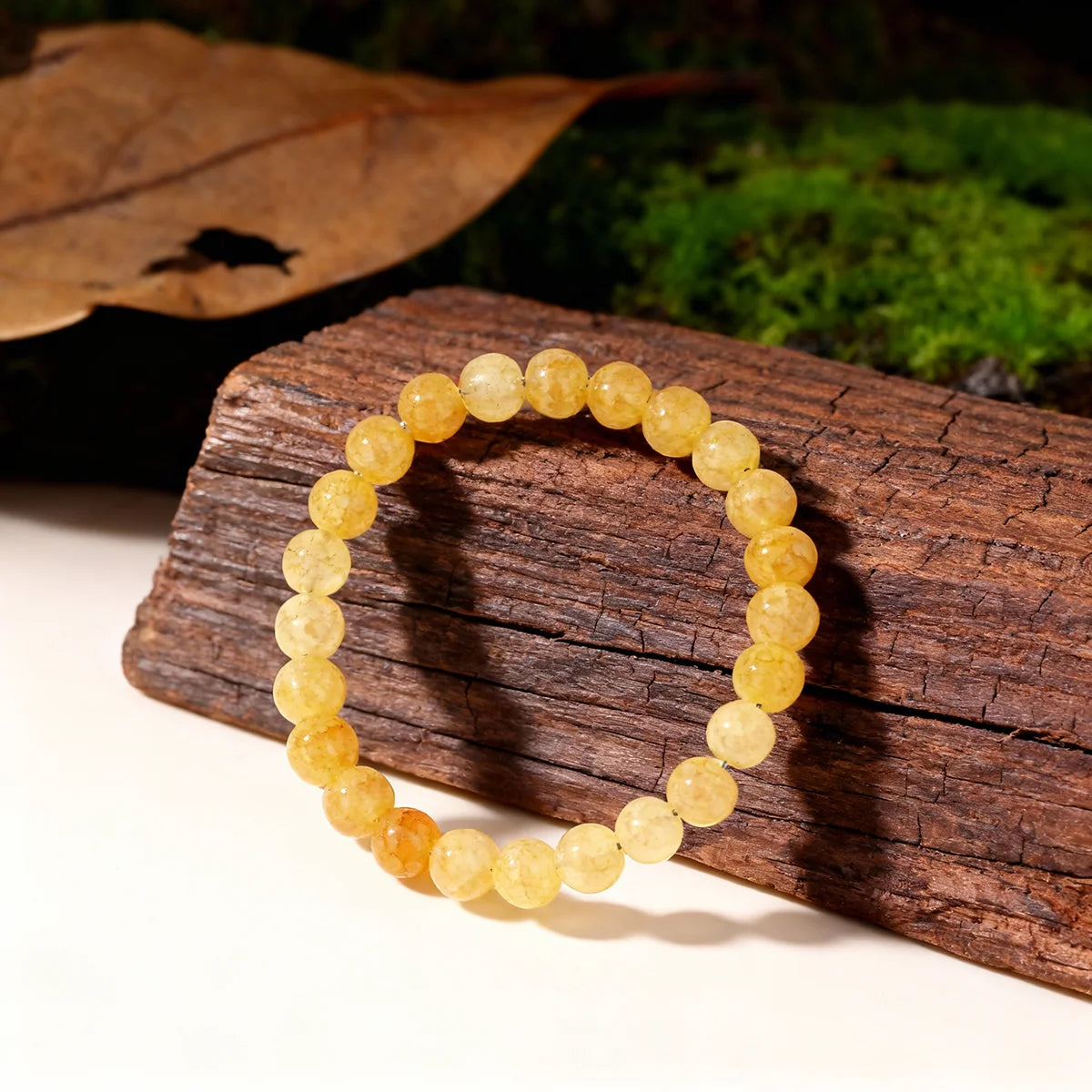 A round bracelet made of yellow citrine crystal beads resting on a piece of dark wood next to green moss.