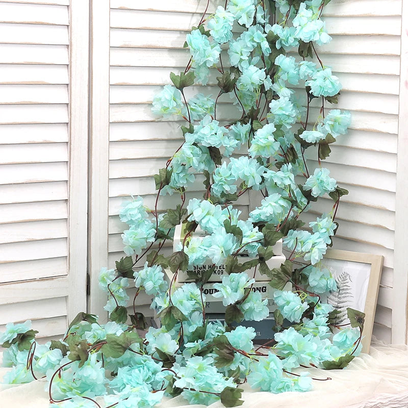 A cascading garland of artificial light blue sakura flowers draped against a white slatted background.