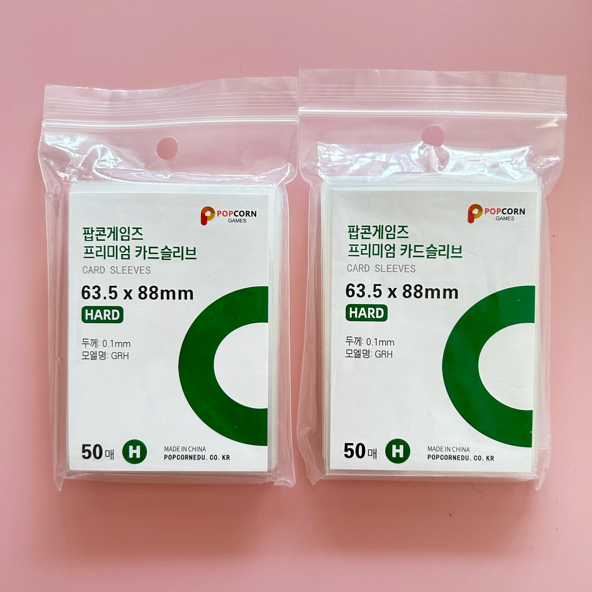 Two sealed packages of POPCORN Games premium card sleeves, 63.5 x 88mm, with green card sleeves visible.