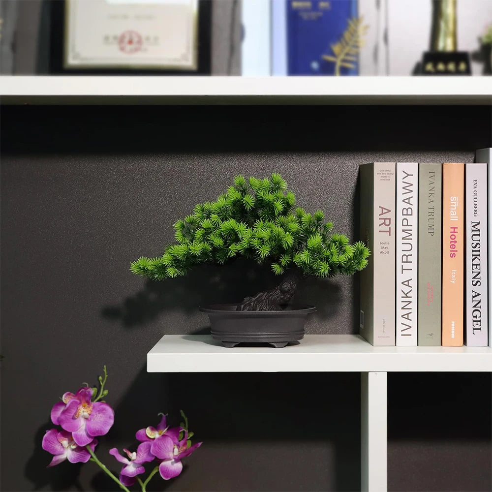 An artificial bonsai tree in a dark pot sits on a white shelf next to books.