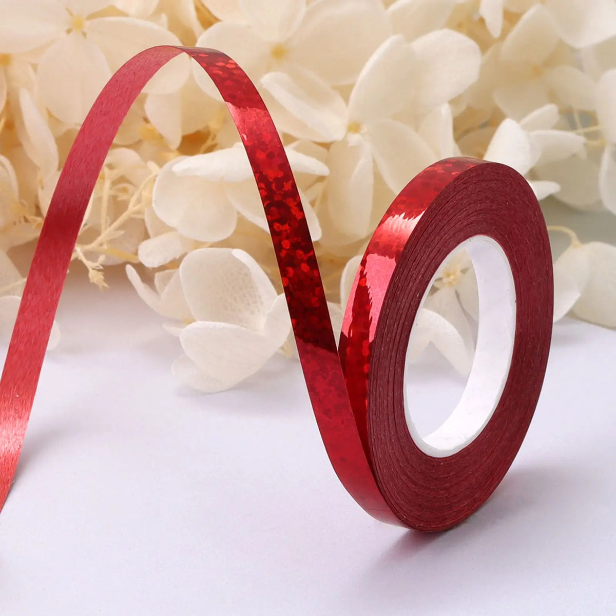 A roll of red glitter satin ribbon unwinding against a background of white flowers.