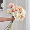 A hand holds a bouquet of artificial Clivia Amaryllis flowers with pink and white petals against a white background.