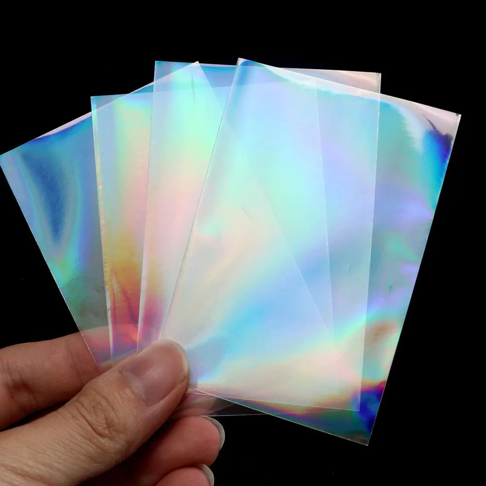 A hand holds a stack of holographic card sleeves, showing iridescent colors and light refraction.