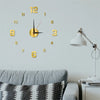 A round gold-colored acrylic digital wall clock with numbers and hands mounted on a light gray wall.