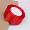 A roll of bright red satin ribbon for crafts and gift wrapping, shown against a light brown paper background.