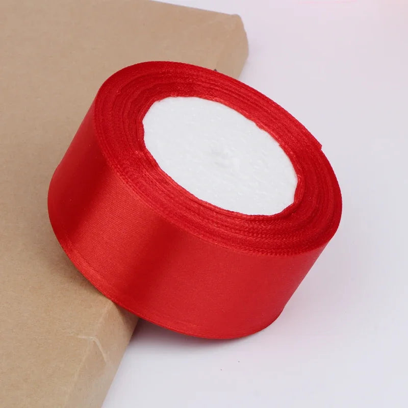 A roll of bright red satin ribbon for crafts and gift wrapping, shown against a light brown paper background.