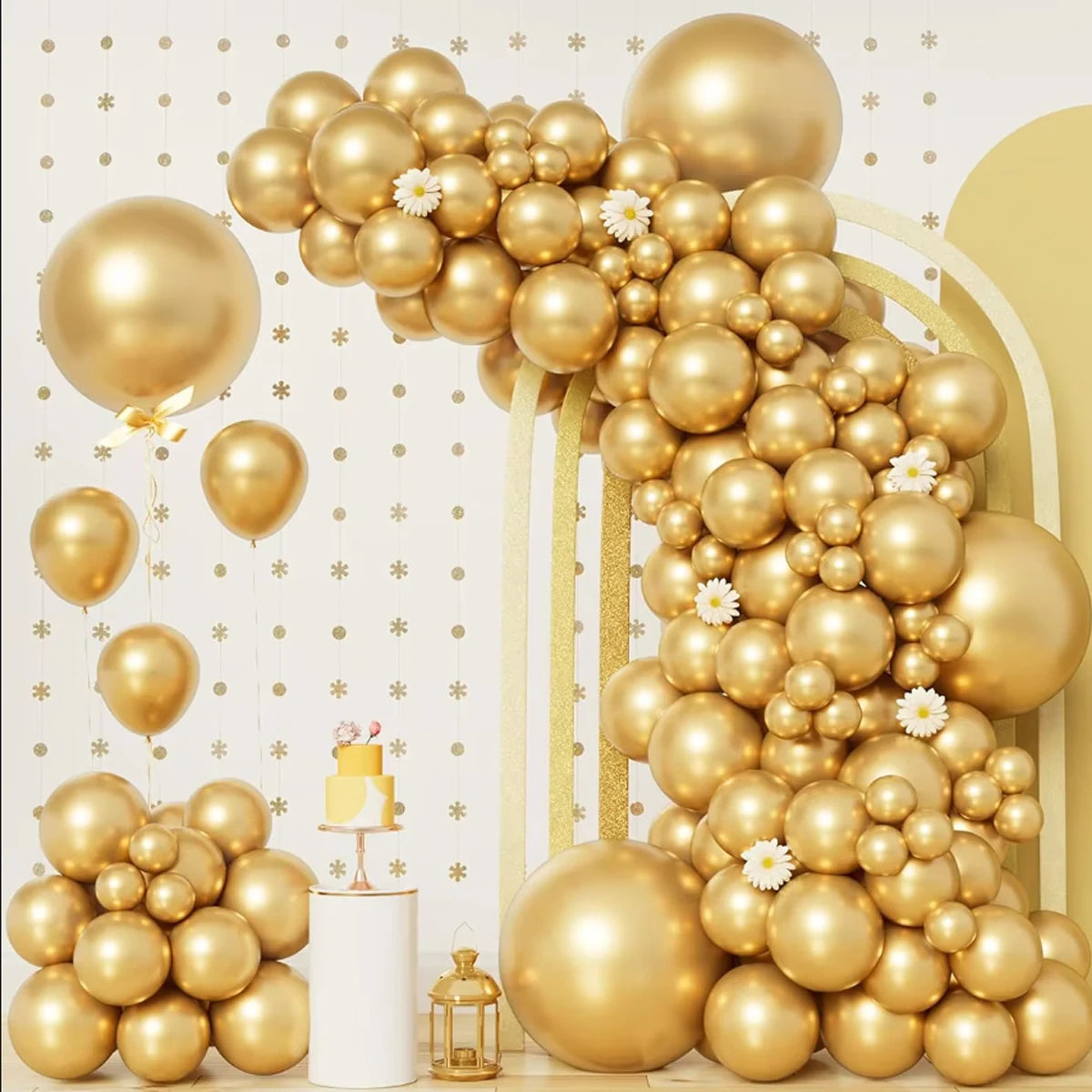 Große goldene Ballon-Girlande mit verschieden großen Ballons und einem mehrstöckigen Kuchen auf weißem Ständer.
