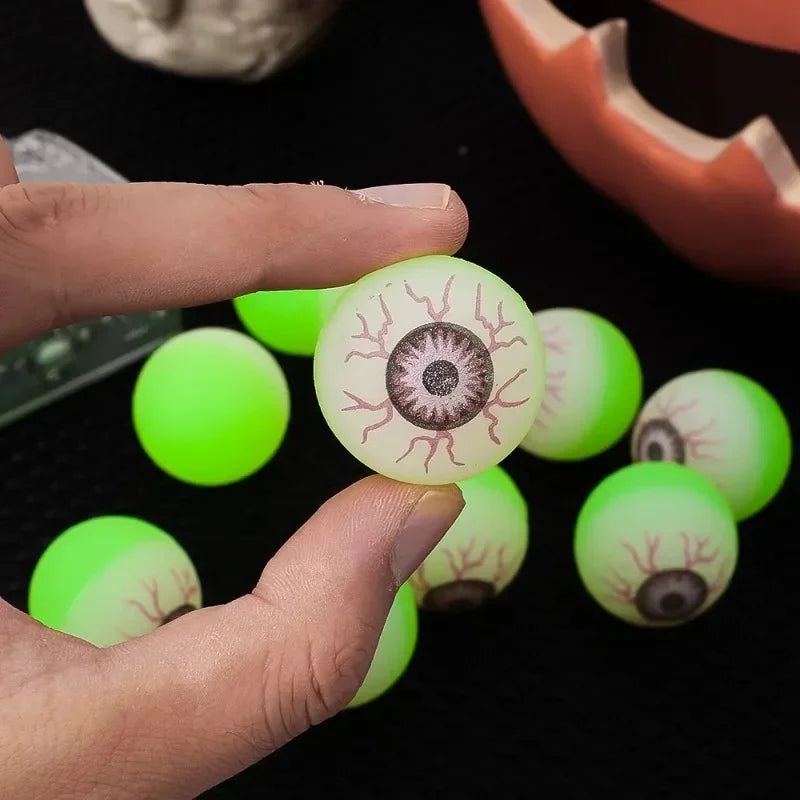 A hand holds several glowing green and yellow glow-in-the-dark eyeball bouncy balls.