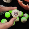 A hand holds several glow-in-the-dark Halloween eyeball bouncy balls against a dark background.