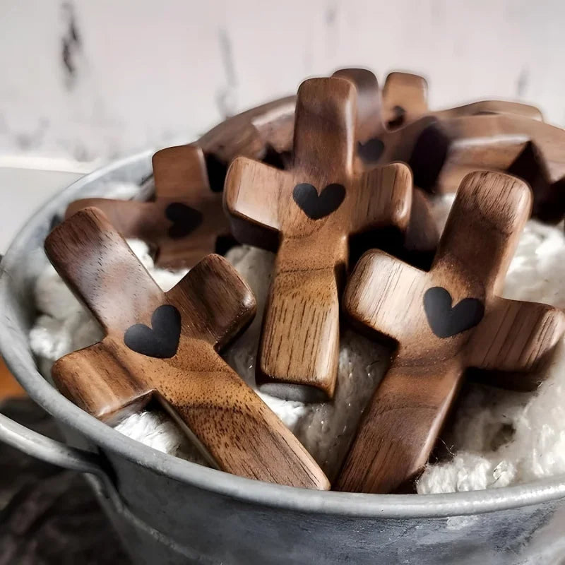 A collection of dark wood comfort prayer crosses with small black hearts floating in white fluffy material.