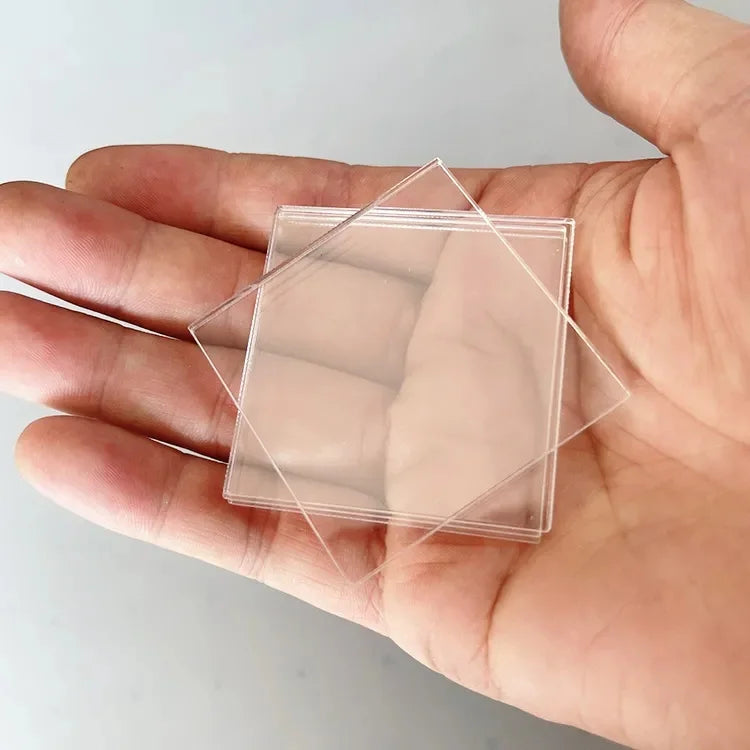 A hand holds a clear square plastic sheet with a diamond-shaped cutout, used for making custom fridge magnets.