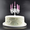 A white birthday cake decorated with light green accents and a silver candelabra holding nine pink candles.