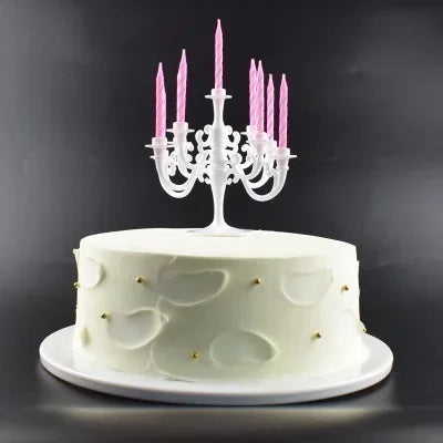 A white birthday cake decorated with light green accents and a silver candelabra holding nine pink candles.