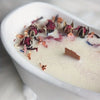 A white ceramic dish holds dried floral elements and a small wooden stick on a surface.