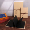 A set of three blank beige scrapbook album covers and a black folder displayed on a wooden surface.