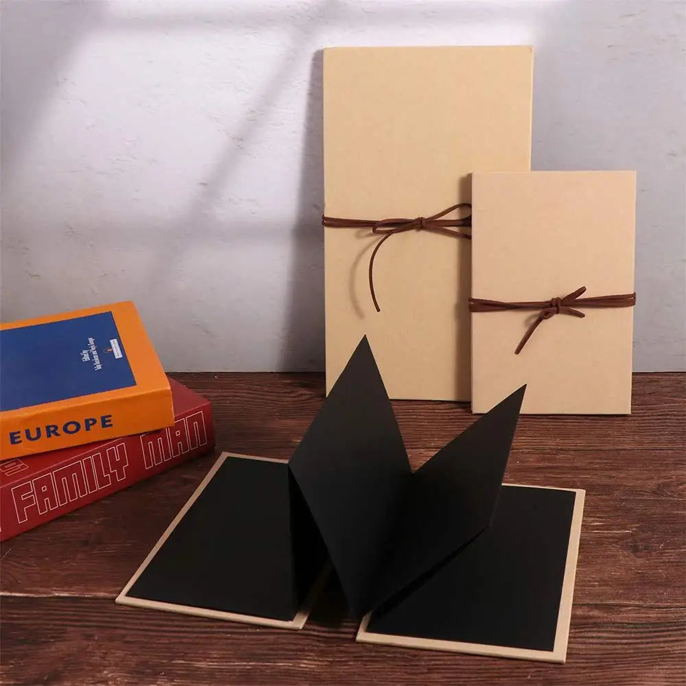 A set of three blank beige scrapbook album covers and a black folder displayed on a wooden surface.