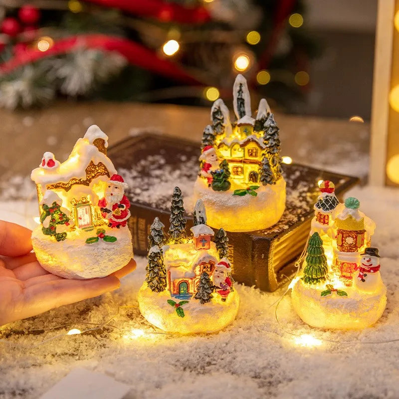 A hand holds a set of illuminated Christmas gingerbread house resin ornaments resting on a snowy surface.
